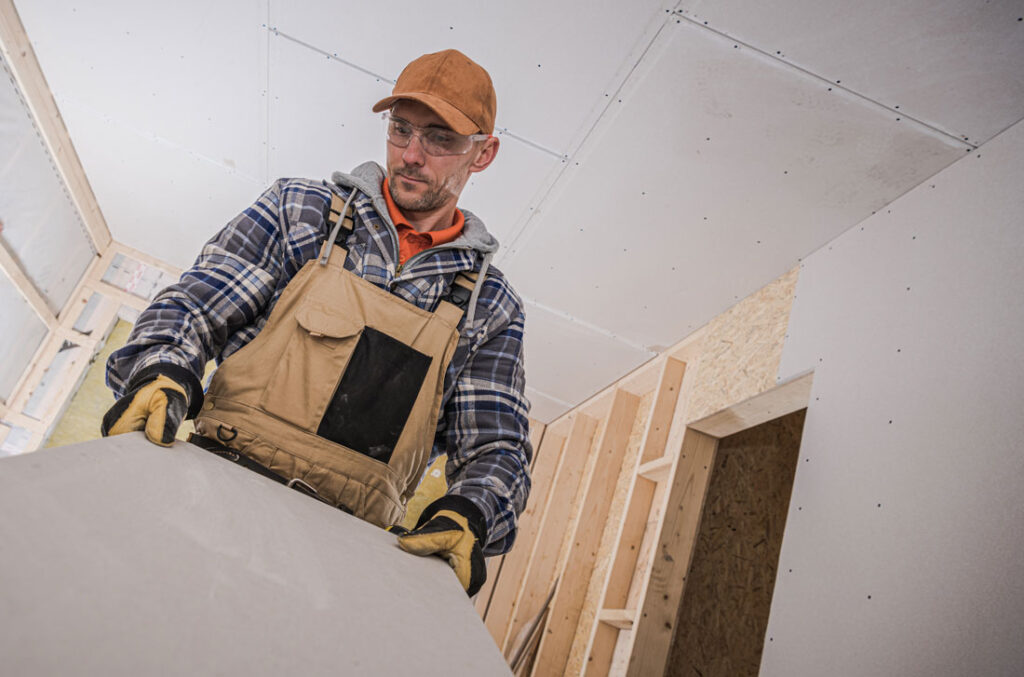 A construction worker carrying a sheet rock drywall for installation for home remodel.