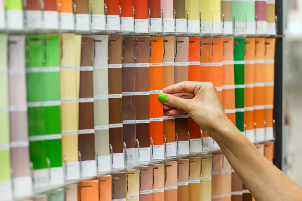 A cropped view of a woman’s hand with green nail polish looking through paint swatches.